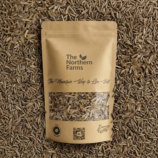 A kraft paper stand-up pouch of The Northern Farms organic chitrali black cumin seeds, placed flat on a bed of loose cumin seeds. The pouch features a clear window showing the dried cumin inside and branding text.