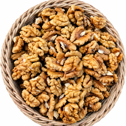 A top-down view of raw, unshelled walnuts piled inside a round woven straw basket on a solid white background.