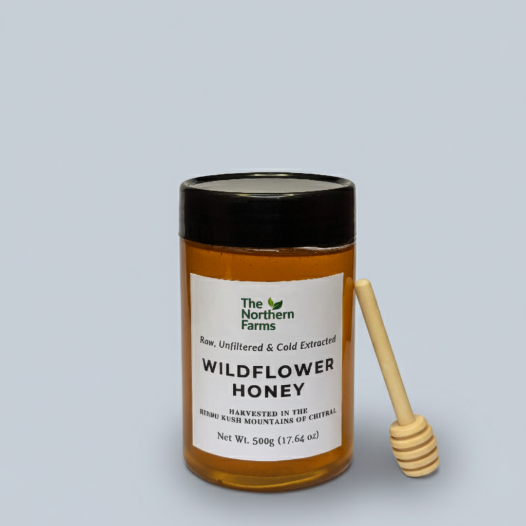 A 500g jar of The Northern Farms Wildflower Honey with a black lid and a wooden honey dipper, set against a solid light gray background.