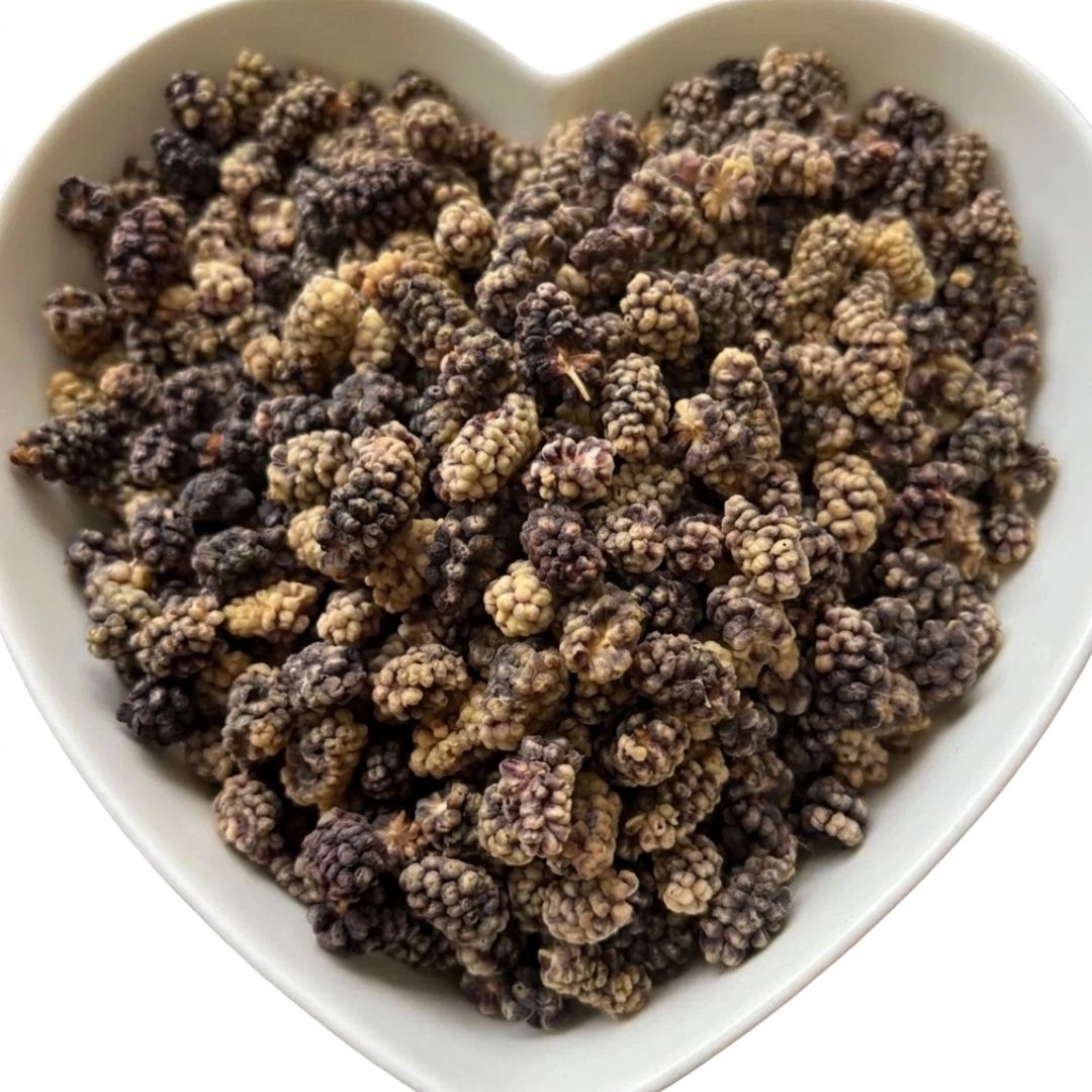 Dried mulberries in dark purple and beige tones piled in a white heart-shaped bowl against a white background.